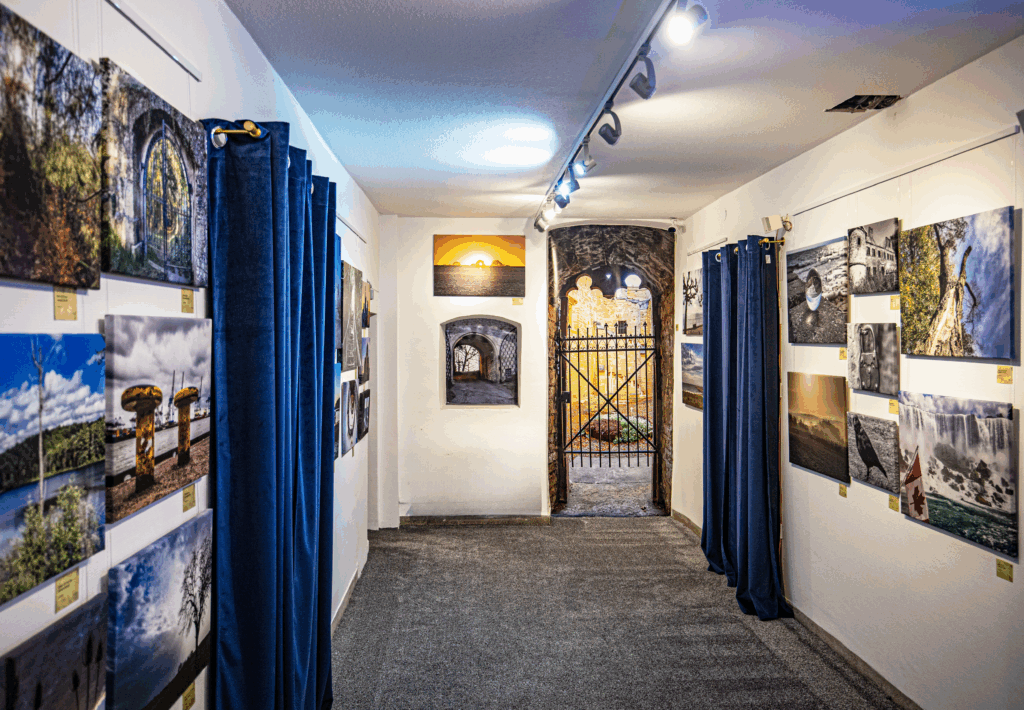 Innenansicht der Galerie Alte Apotheke in Schramberg mit ausgestellten Fotografien von Thomas Klukas auf Leinwand, Acrylglas und Alu Dibond; Blick durch den Raum auf ein Tor mit warmem Licht im Hintergrund.